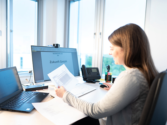 Eine Frau sitzt am Schreibtisch und prüft Unterlagen.