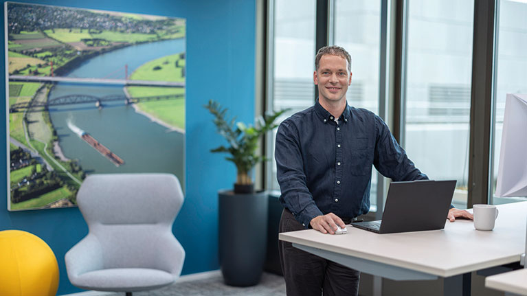 Felix steht an einem Hubschreibtisch mit aufgeklapptem Laptop.