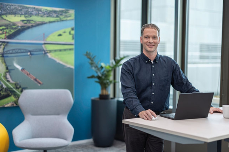 Felix steht an einem Hubschreibtisch mit aufgeklapptem Laptop.