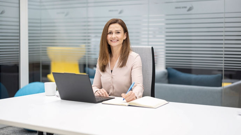 Judith hat ihren Laptop in einem hellen Büro vor sich aufgeklappt und macht sich Notizen.