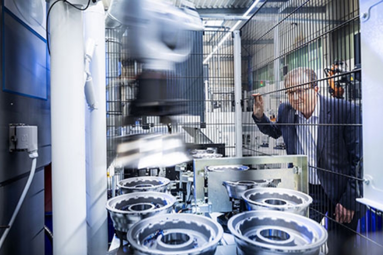 Ein Mann beobachtet durch einen Zaun die maschinelle Produktion von Getriebeteilen