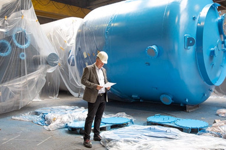 Dr. Jörg Doege, Geschäftsführer von Inprocoat, mit Schutzhelm vor einem Metalltank in einer Werkshalle