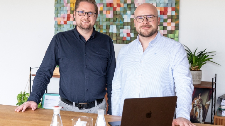 Dr. Tobias Börnhorst (l., CTO) und Steffen Gerlach (CEO) sind Gründer des Start-ups eeden und stehen vor einem bunten Bild an einem Schreibtisch
