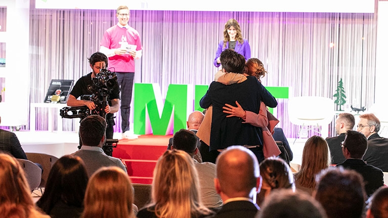 Auf einer Bühne umarmen sich zwei Personen vor Publikum, während Kamerateam und Moderation die Preisverleihung von MUT - DER GRÜNDUNGSPREIS begleiten.