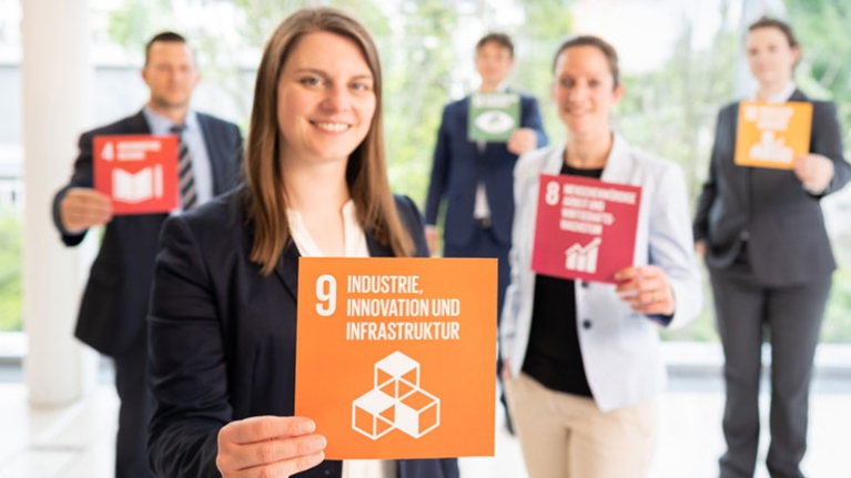 Mehrere Menschen halten Karten in die Kamera, nur die vorderste ist lesbar: Industrie, Innovation und Infrastruktur