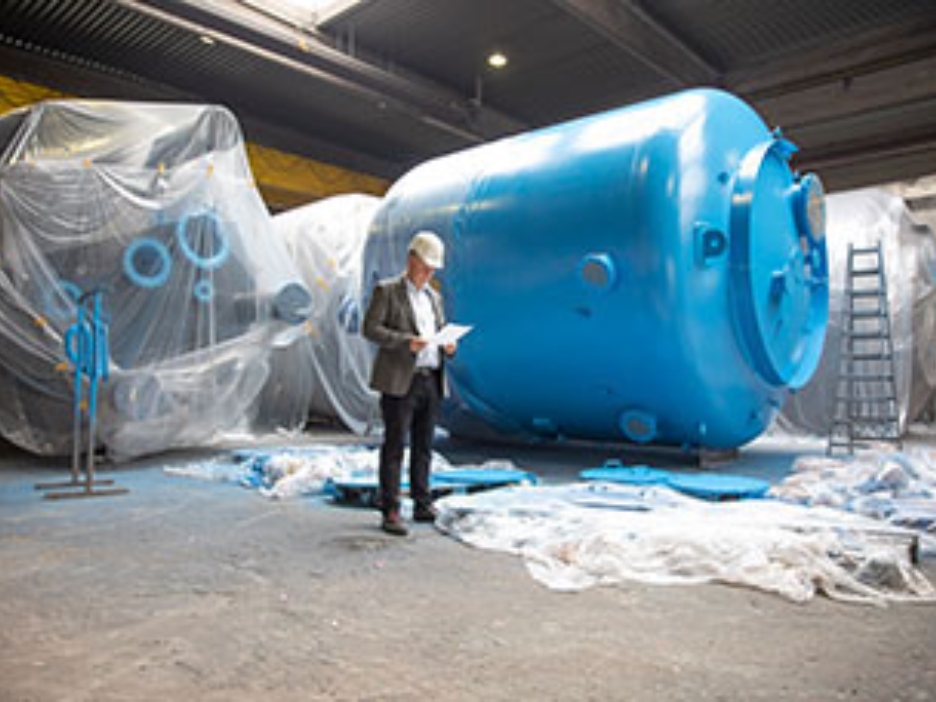 InProCoat-Geschäftsführer Dr. Jörg Doege in einer Werkshalle vor einem großen blauen Metalltank