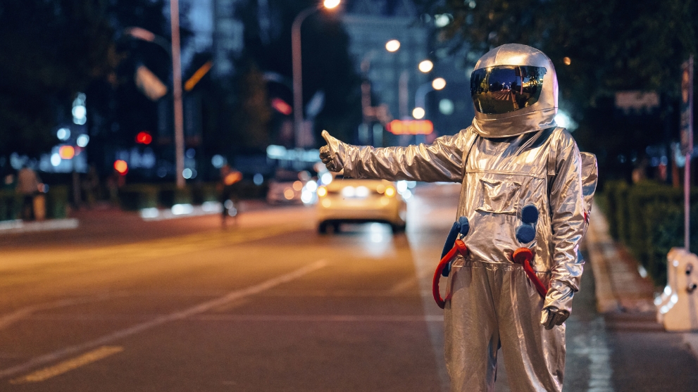 Mann in einem Astronautenanzug in Anhalterpose an einer Straße