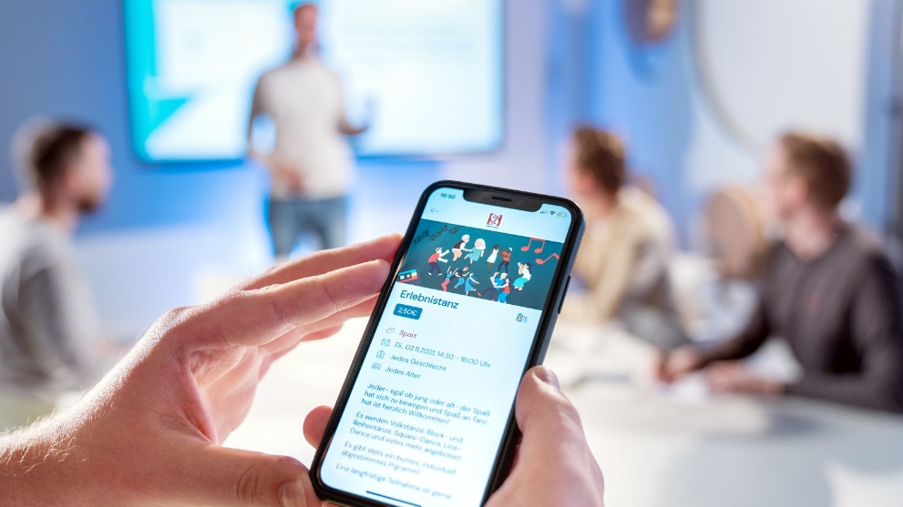 Ein Mann hält ein Handy, auf dem ein Kurs zu einem Erlebnistanz angezeigt wird