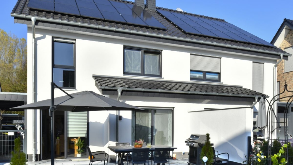 Ein weißes Einfamilienhaus mit schwarzem Dach, auf dem Solarpanel installiert sind.