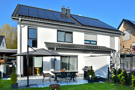 Ein weißes Einfamlienhaus mit schwarzem Dach, auf dem Solarpanel installiert sind.