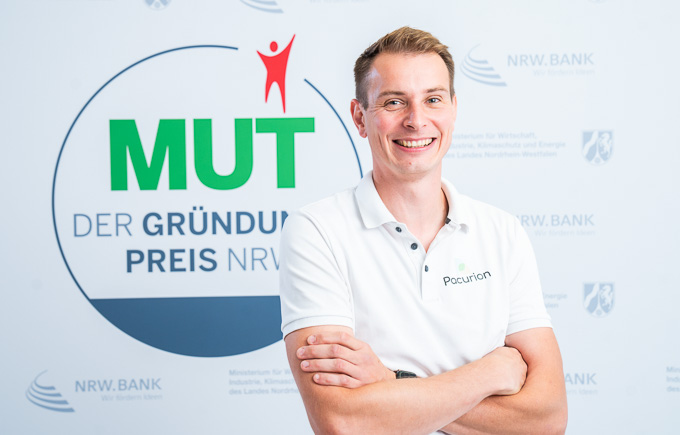 Dominik Leufgen von Pacurion vor dem MUT - DER GRÜNDUNGSPREIS NRW-Logo