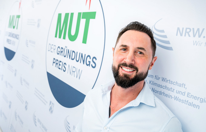 Robin Klein von Pader Solartechnik vor dem MUT - DER GRÜNDUNGSPREIS NRW-Logo