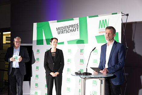 Norbert Tiemann, NRW-Landwirtschaftsministerin Silke Gorißen und Michael Block stehen vor einer Logowand. Michael Block hält eine Laudatio.