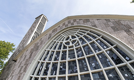 Graue Stein-Fassade einer Kirche mit geschwungener Fensterfront aus der Froschperspektive