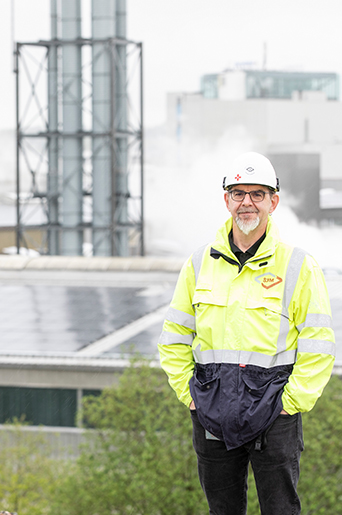 Andreas Fedderwitz, Elektroingenieur bei dem Recyclingbetrieb, steht in gelber Warnjacke auf einer Anhöhe vor den Fabrikdächern mit Solarmodulen