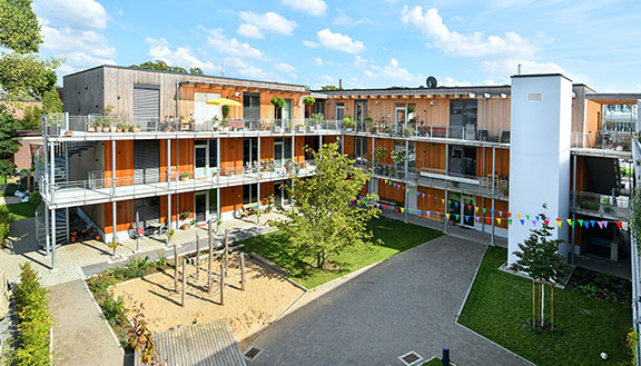 Innenhof des Wohnprojekts TRIALOG in Hilden mit Spielplatz und bunten Fahnengirlanden.