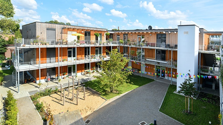 Innenhof des Wohnprojekts TRIALOG in Hilden mit Spielplatz und bunten Fahnengirlanden.