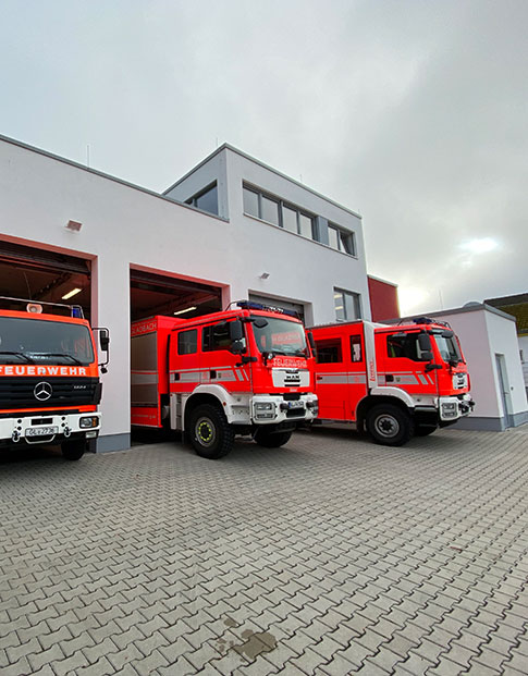 Drei Feuerwehrautos stehen in den Einfahrten eines Feuerwehrhauses