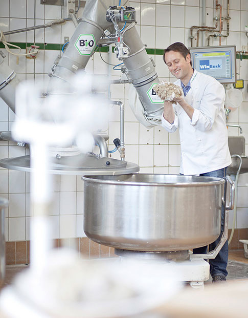 Bäcker Roland Schüren vor einer Knetmaschine in seiner Backstube. Er begutachtet den Teig.