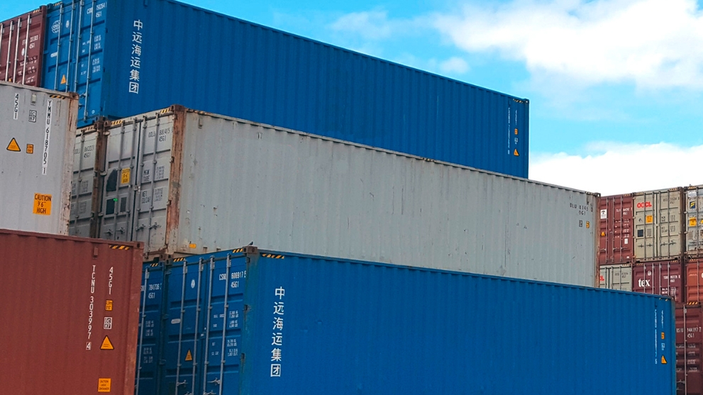 Mehrere verschiedenfarbige Schiffscontainer, die in einem Hafen gestapelt sind.