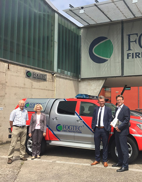Drei Männer und eine Frau vor einem Einsatzfahrzeug auf dem Parkplatz des Brandschutzunternehmens FOGTEC