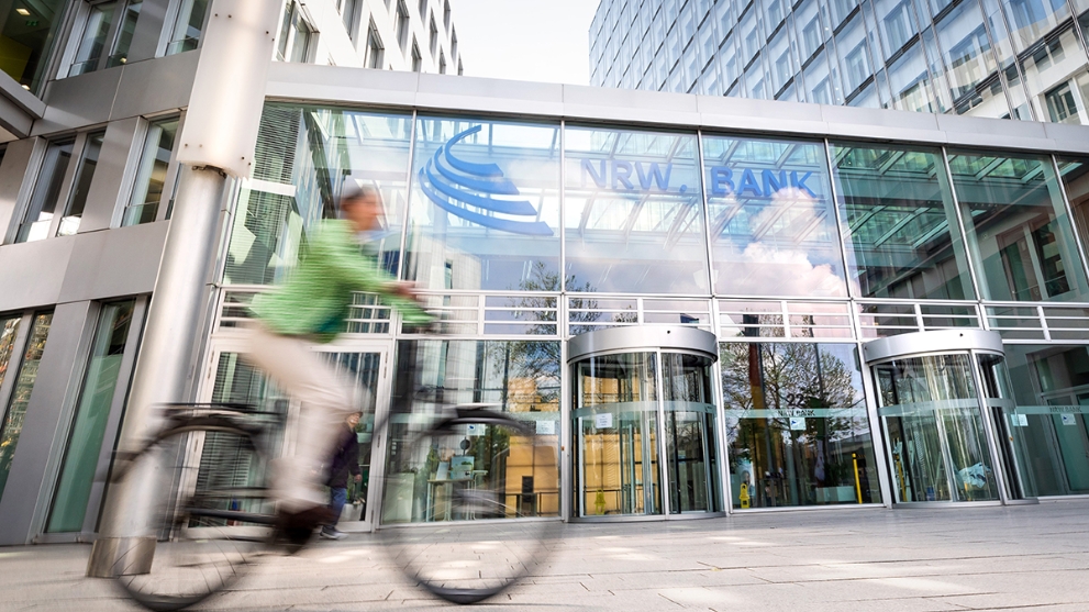 Fahrradfahrerin vor dem gläsernen Eingangsbereich der NRW.BANK-Zentrale in Düsseldorf