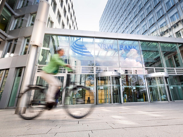 Fahrradfahrerin vor dem gläsernen Eingangsbereich der NRW.BANK-Zentrale in Düsseldorf