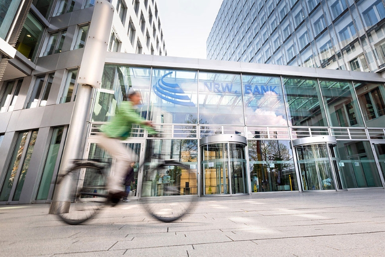 Fahrradfahrerin vor dem gläsernen Eingangsbereich der NRW.BANK-Zentrale in Düsseldorf