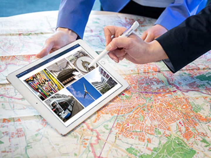 Auf einer Landkarte liegt ein Tabletcomputer, darauf Fotos verschiedener Förderprojekten der NRW.BANK