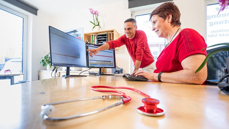 Sascha Jung und eine Mitarbeiterin vor zwei Computerbildschirmen