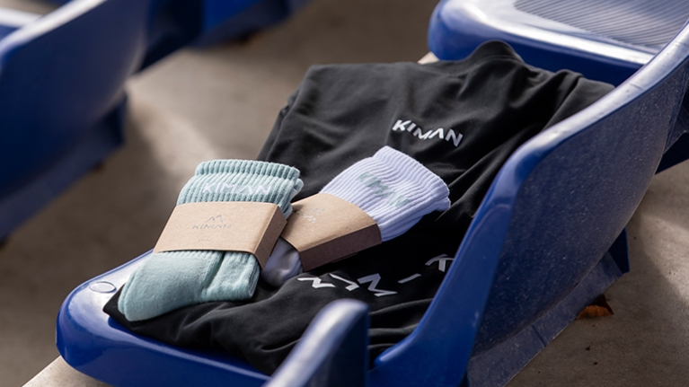 Gefaltetes schwarzes T-Shirt und zwei Paar Socken mit Papierband liegen auf blauen Stadionsitzen.