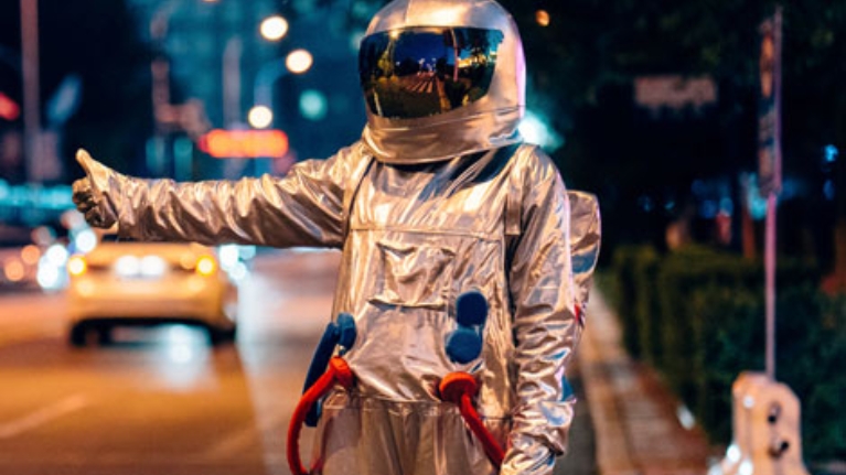 Mann in einem Astronautenanzug in Anhalterpose an einer Straße