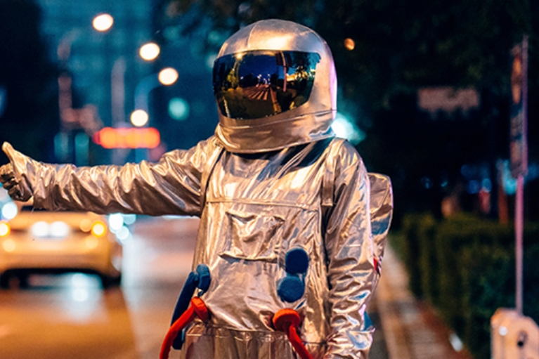 Mann in einem Astronautenanzug in Anhalterpose an einer Straße