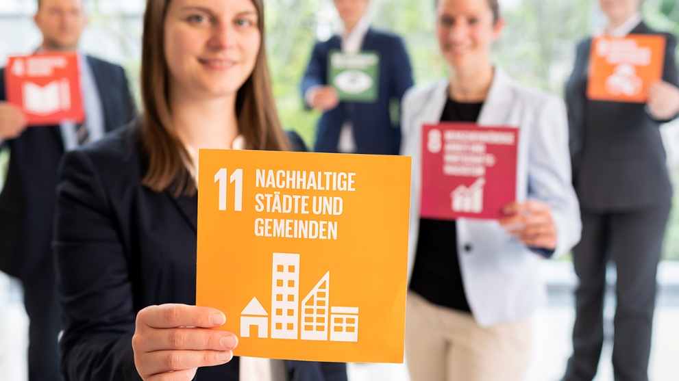 Mitarbeiter der NRW.BANK halten Karten mit Symbolen der Sustainable Development Goals hoch.