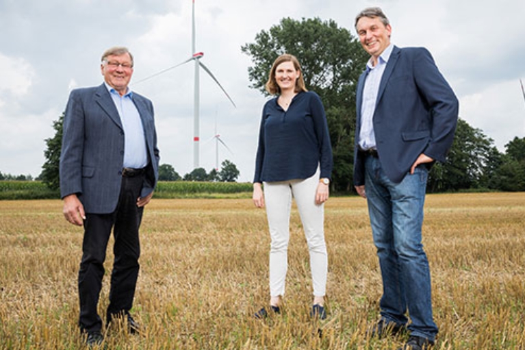 Bernhard Wieker, Theresa Ungru und Hermann Willers von der Hörstel GmbH & Co. KG stehen vor einer Windkraftanlage.