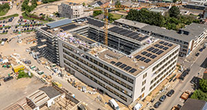 Luftaufnahme einer großen Rathaus-Baustelle mit Kran und umliegender Stadtinfrastruktur.